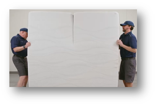 Two people carrying the mattress upright to set aside