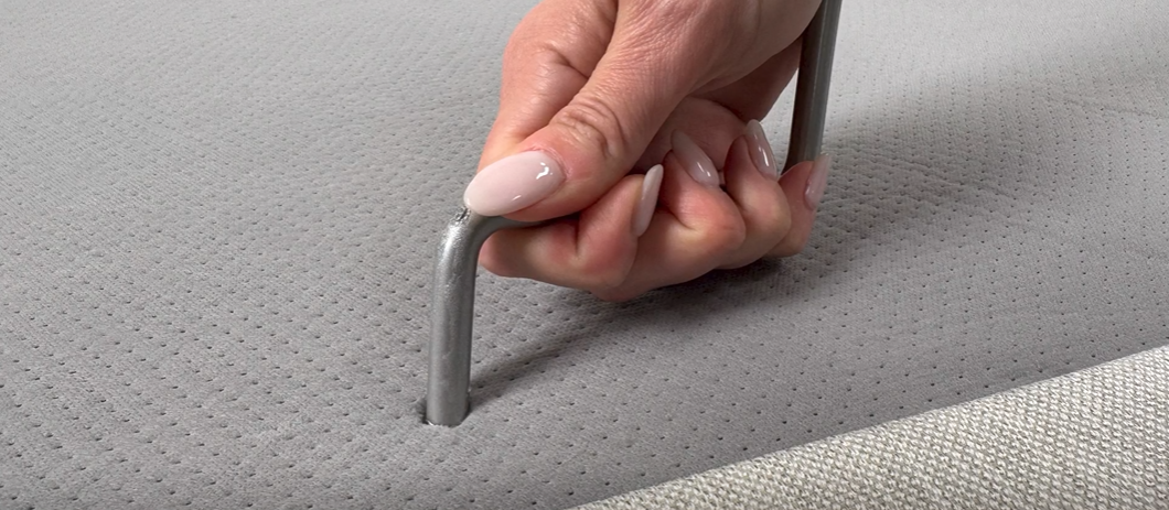 Close-up of a hand gripping a retainer bar inserted into a gray perforated fabric surface.