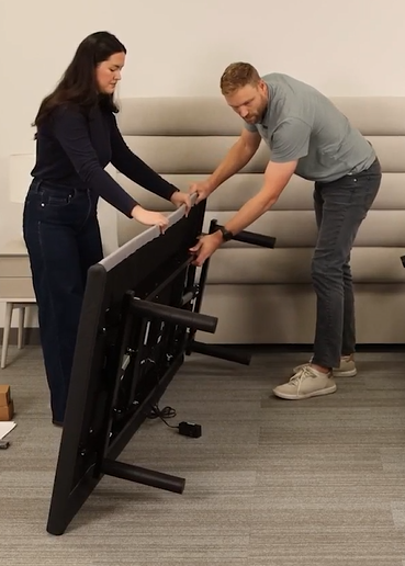 A picture of 2 people placing the adjustable base on it's side.